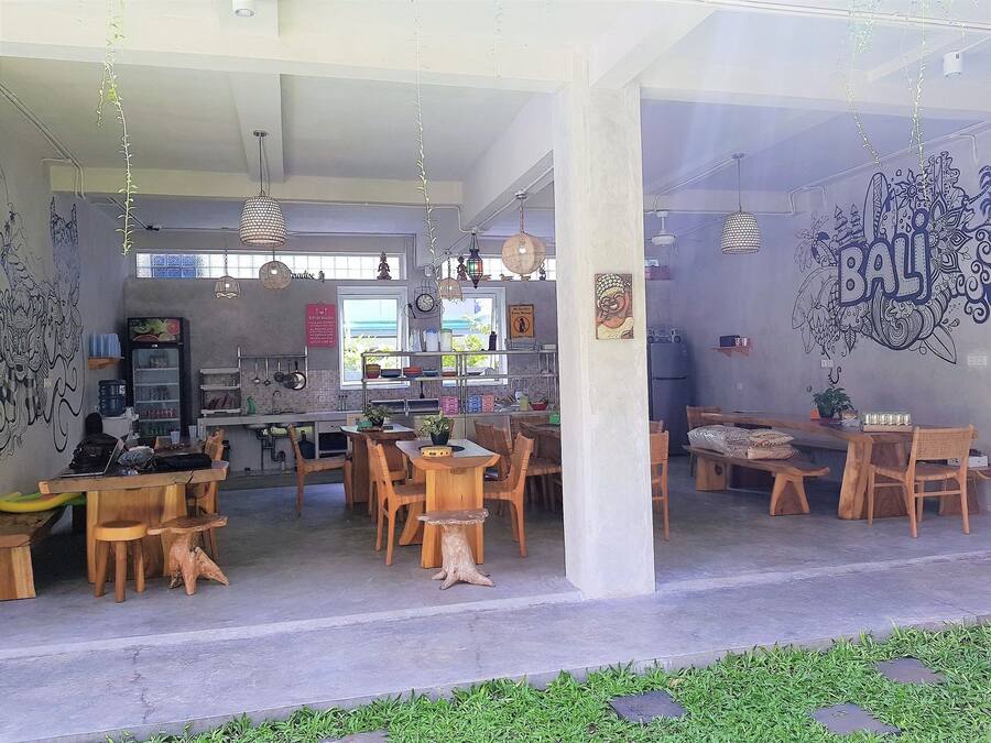 A restaurant with a casual dining setup, including wooden tables and chairs, hanging lights, and a mural on the wall.
