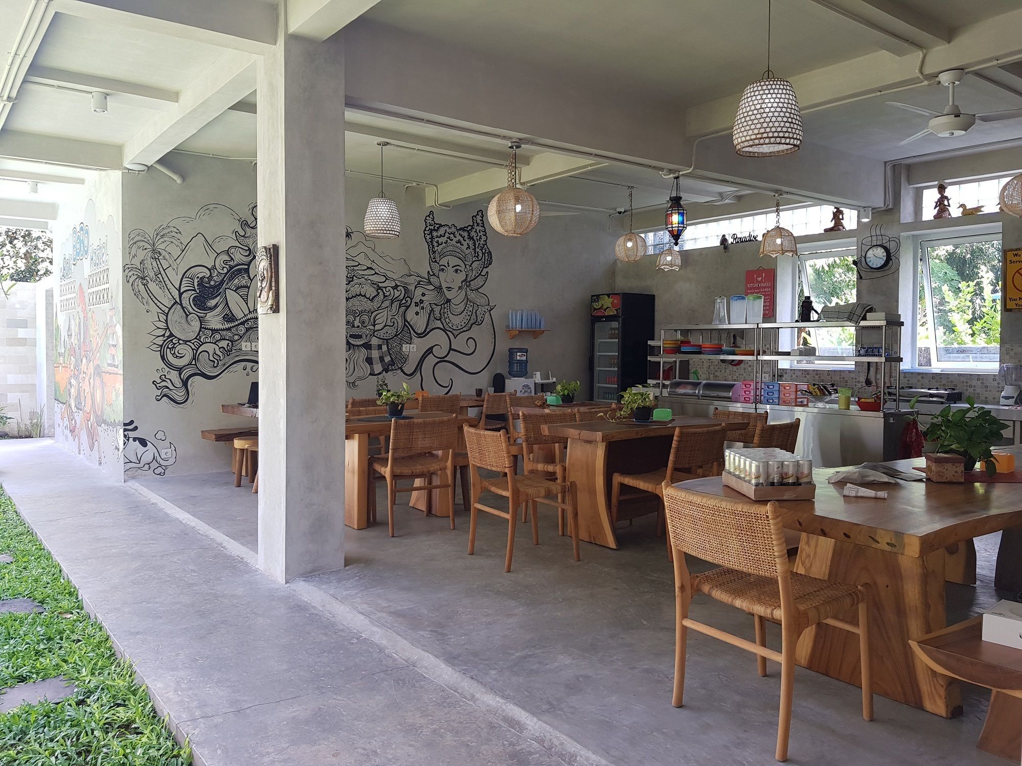 A modern dining area with wooden tables and chairs, decorative wall murals, and hanging pendant lights.