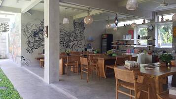 A modern dining area with wooden tables and chairs, decorative wall murals, and hanging pendant lights.
