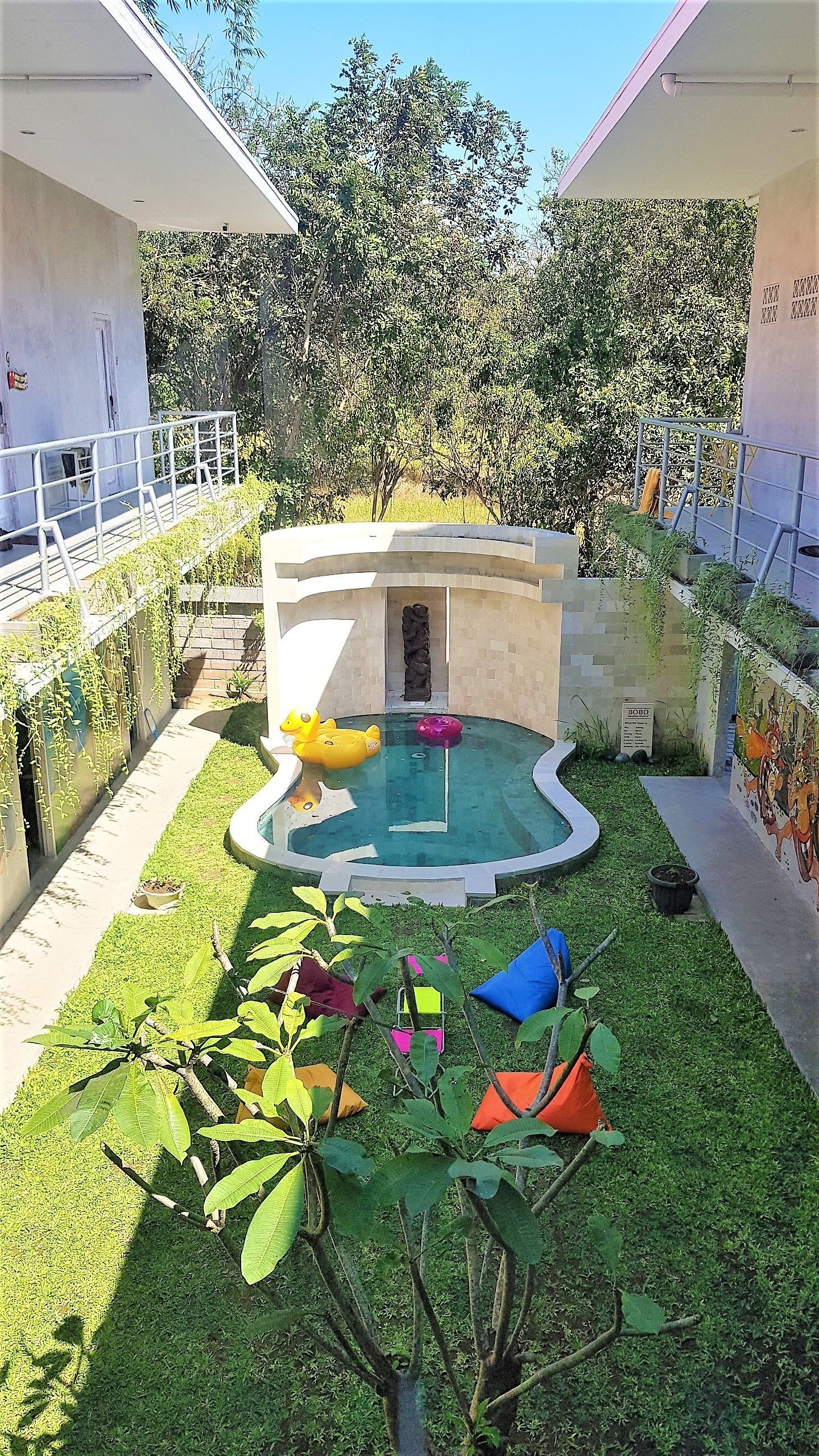 A swimming pool with inflatable toys, surrounded by a grassy area and a small garden.