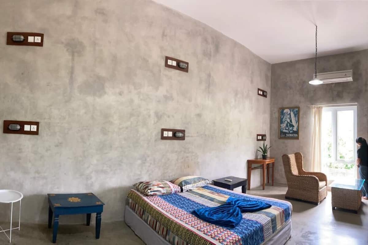 Ein Schlafzimmer mit einem Bett, einem kleinen Tisch, einem Stuhl, einer Pendelleuchte und einem Fenster.