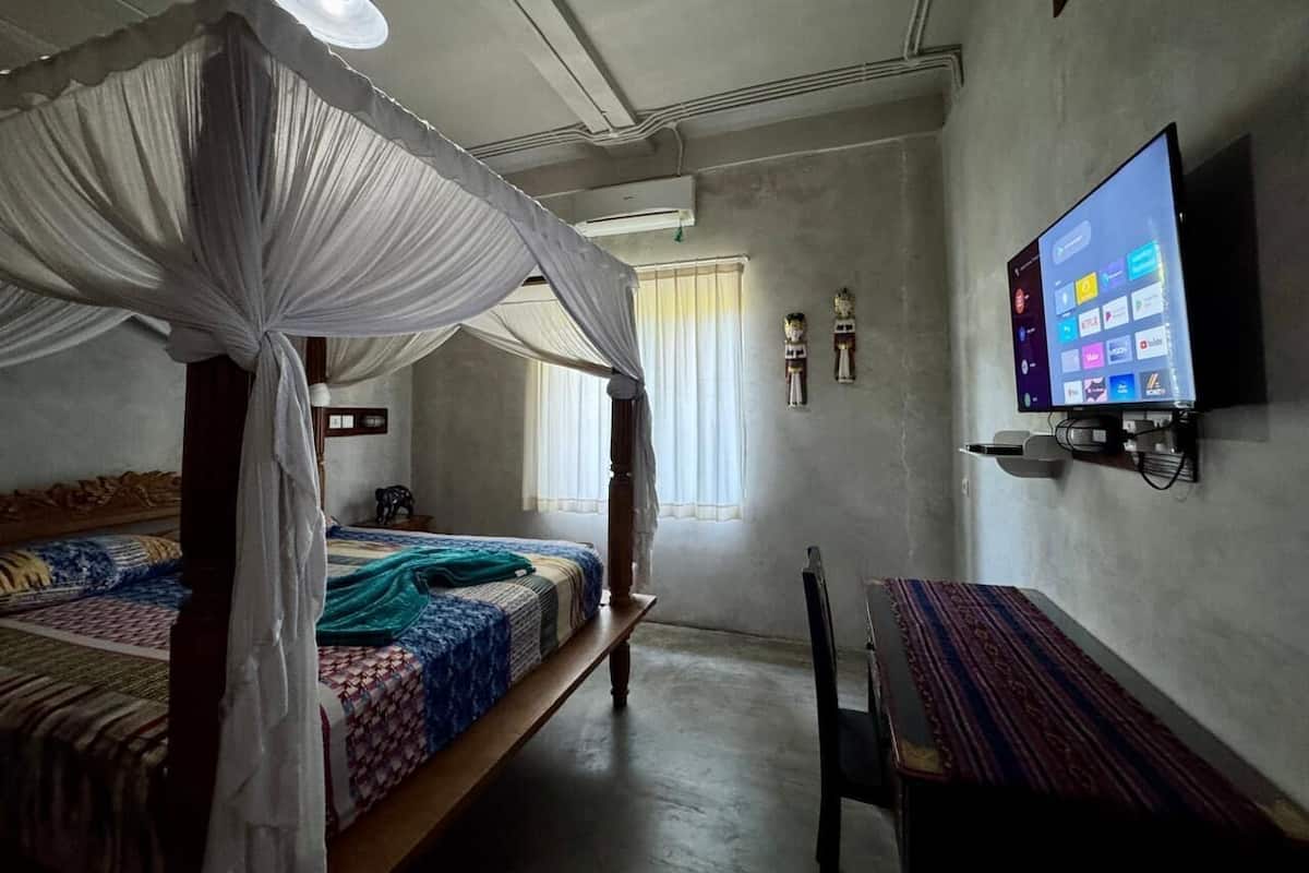Ein Schlafzimmer mit Himmelbett, Wand-Fernseher und Schreibtisch mit Stuhl.