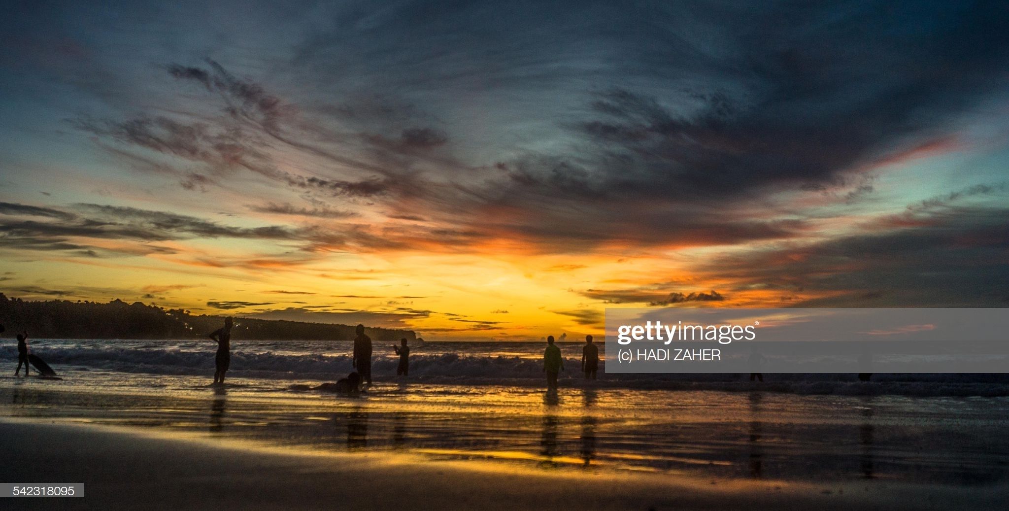 A beach at sunset with silhouettes of people and a dog.