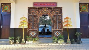 A traditional Balinese Bobo Hostel entrance with ornate decorations, two large umbrellas, and potted plants. - Bali Bobo Hostel (Jimbaran)