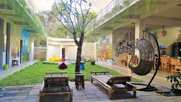 A courtyard with a tree, benches, a hanging chair, and a mural.