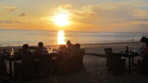 A sunset over the ocean with people dining at tables on the beach. - Bali Bobo Hostel (Jimbaran)