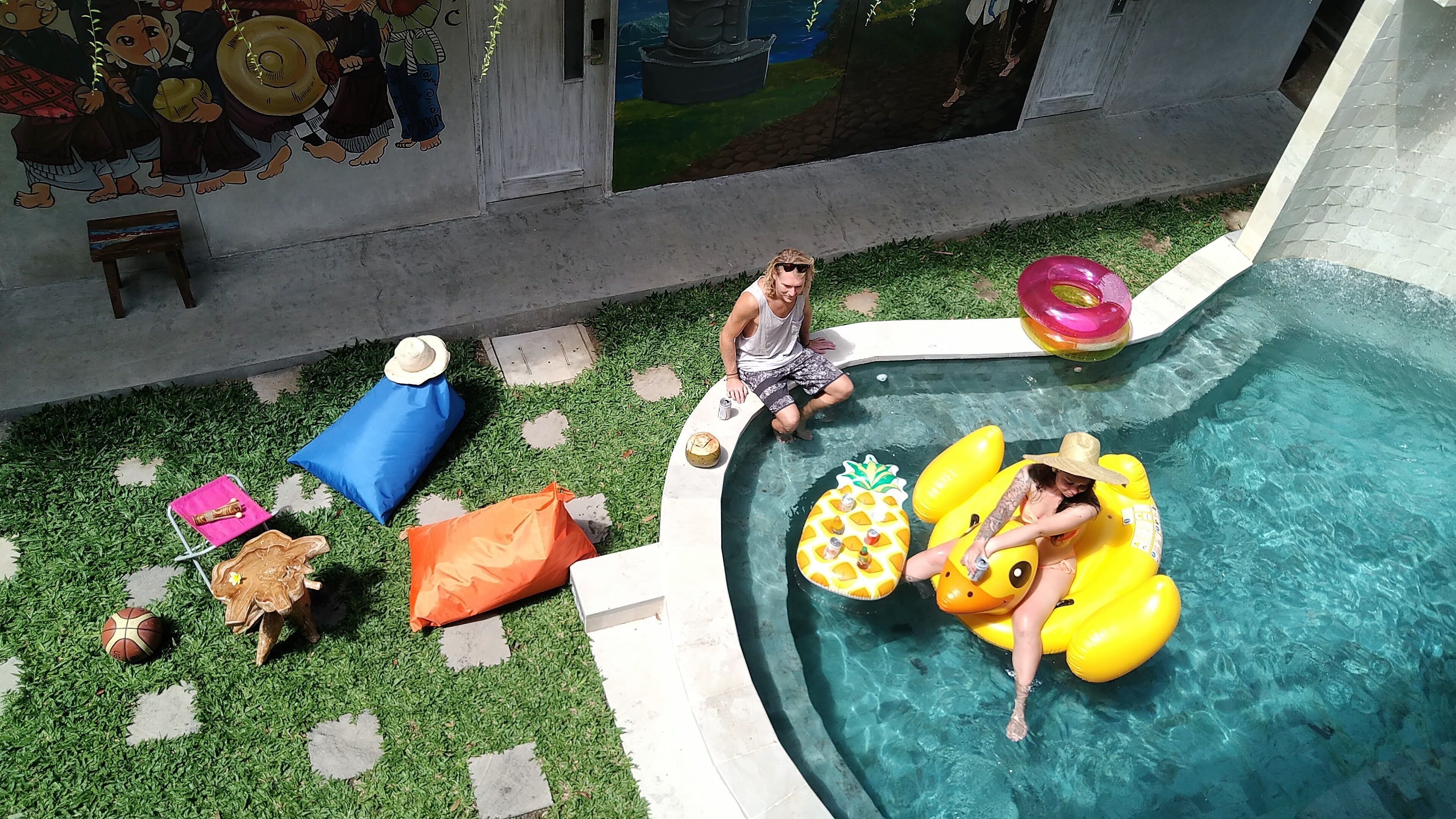 A swimming pool with inflatable toys, a mural on the wall, and a small table with a drink.