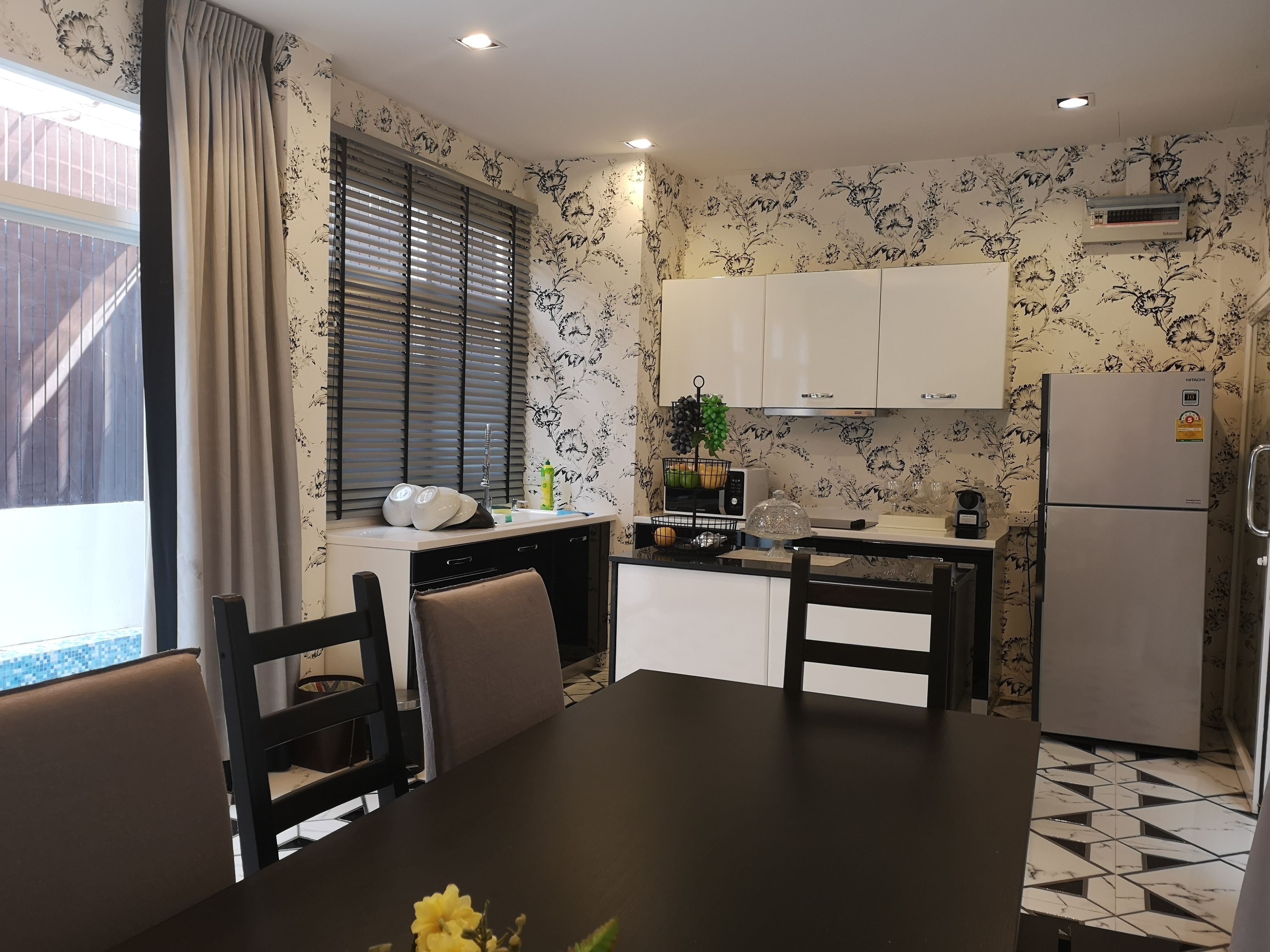 A compact kitchen with a dining table, chairs, a refrigerator, and a window with blinds.