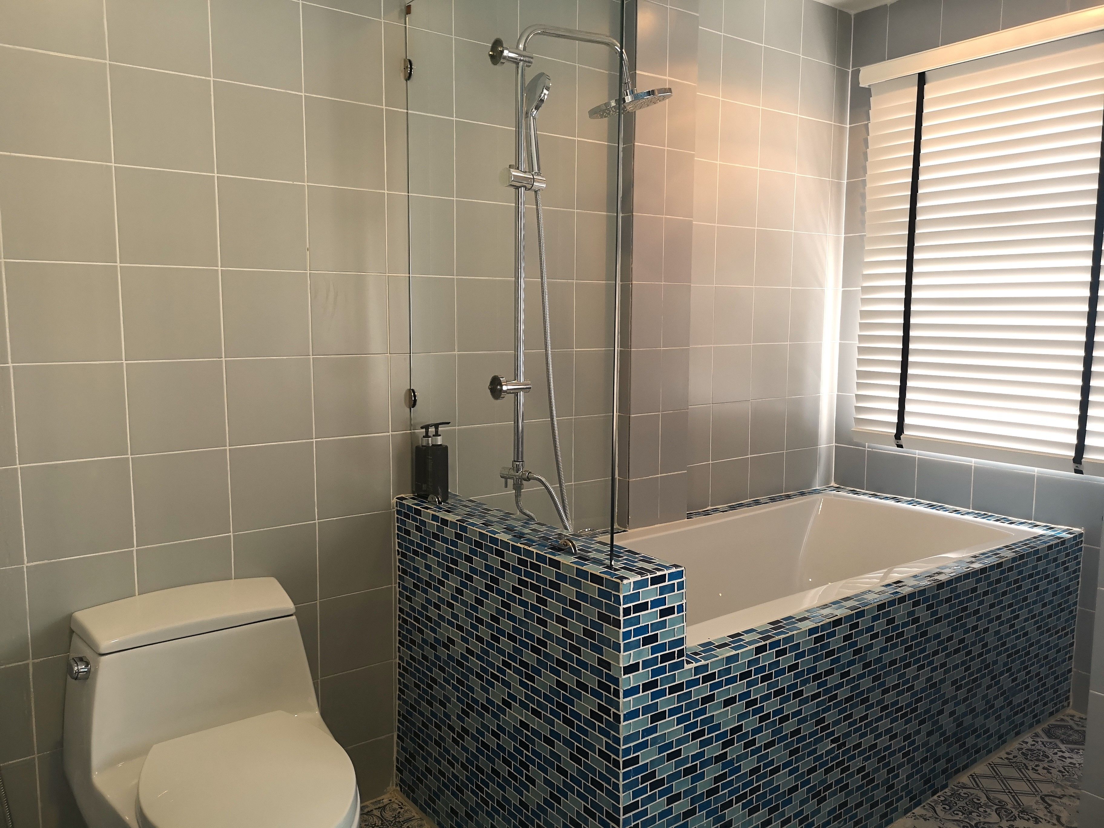 A bathroom with a toilet, a shower with a glass enclosure, and a bathtub with blue mosaic tiles.