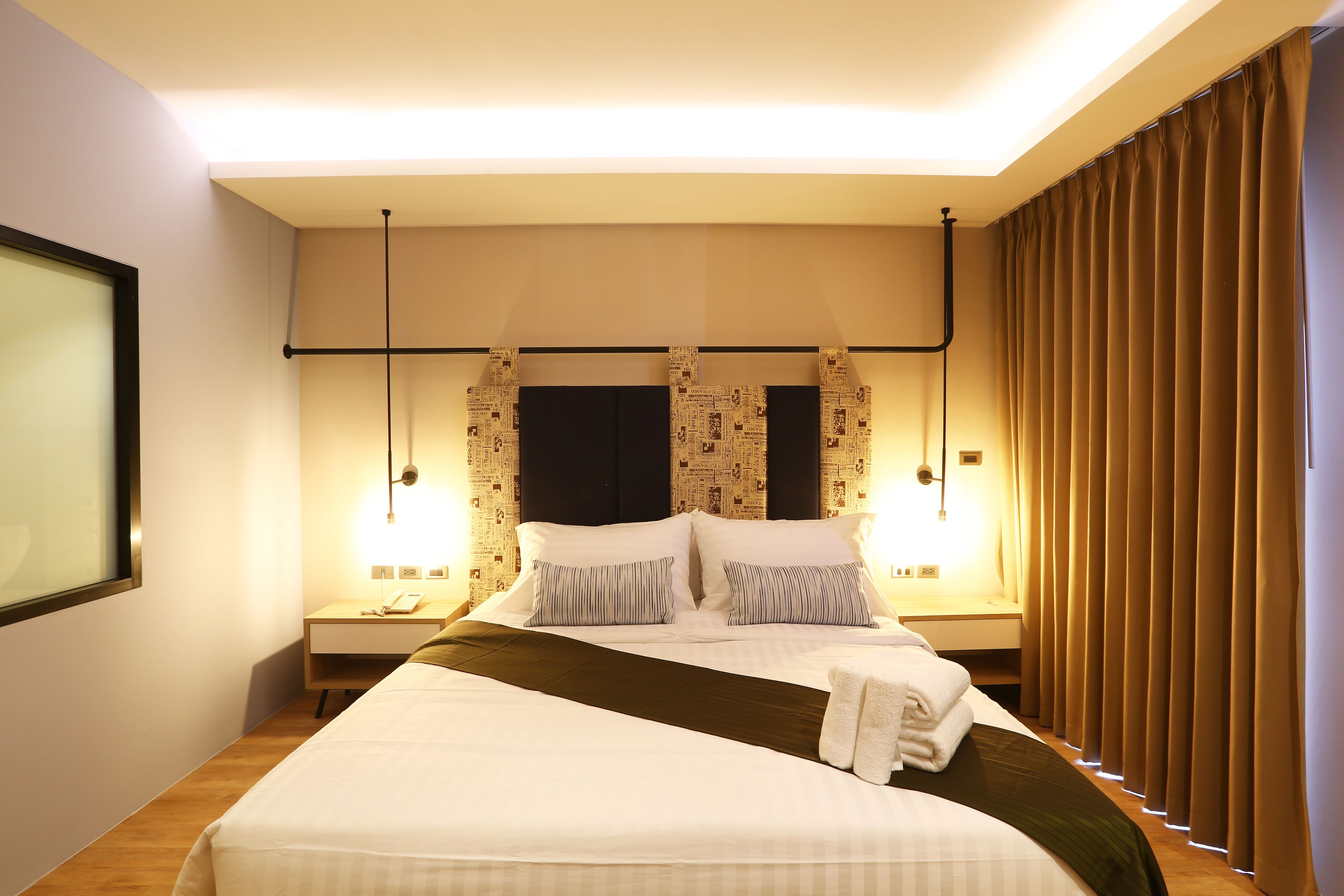Ein Hotelzimmer mit einem großen Bett, zwei Nachttischen, einem Wandfernseher und einem Fenster mit Vorhängen.