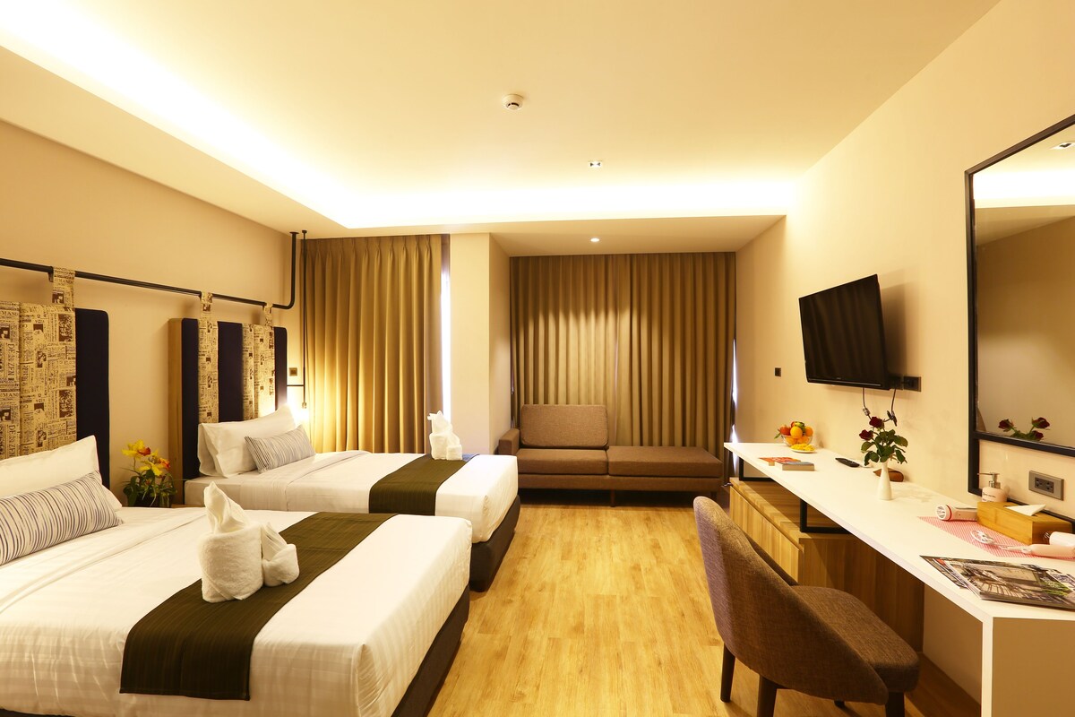 A hotel room with two beds, a desk, a chair, a sofa, a television, and a mirror.