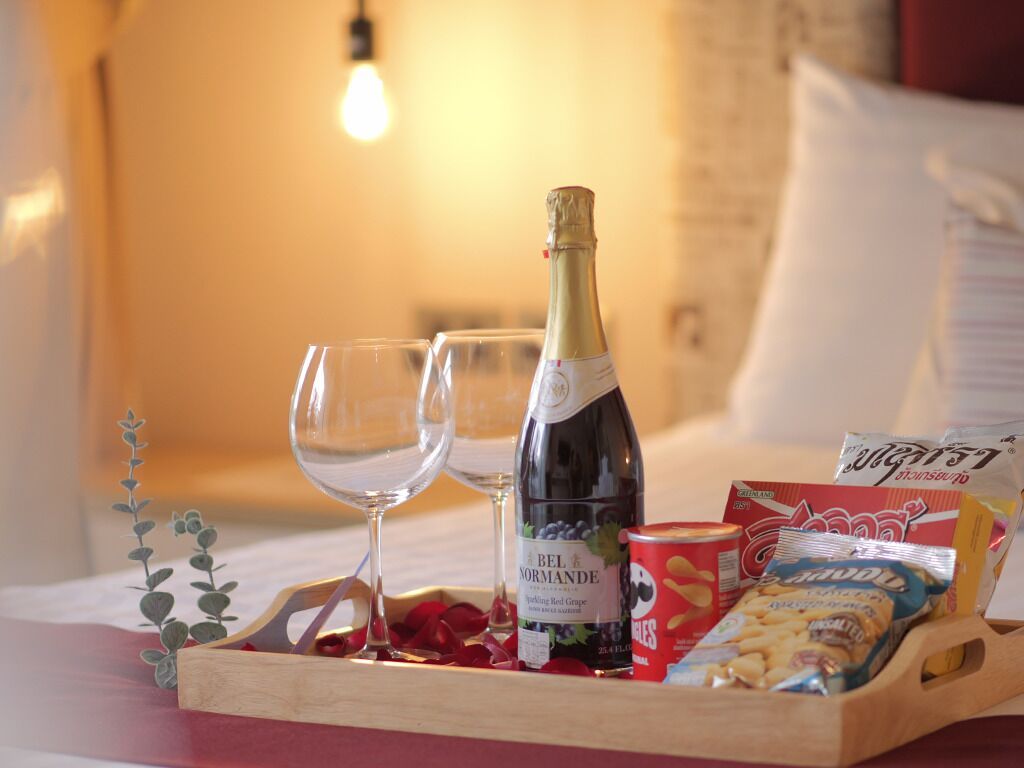 A tray with a bottle of Bel Normande wine, two glasses, and snacks on a bed.