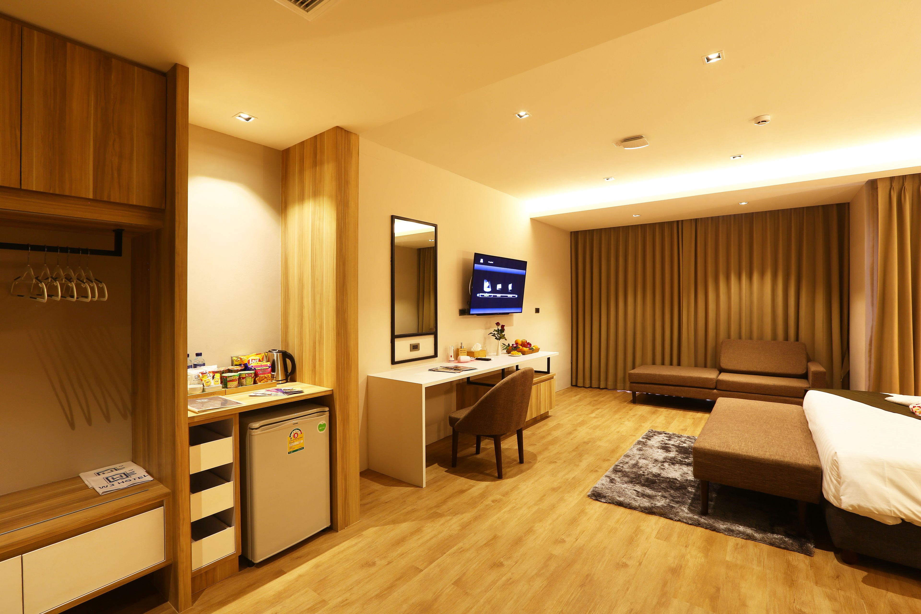 A hotel room with a wooden desk, a small refrigerator, a television, a sofa, and a bed.
