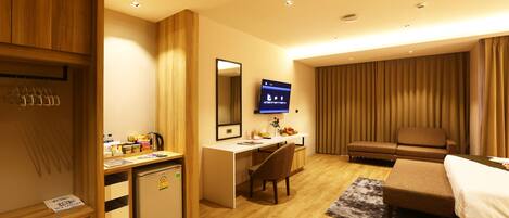 Una habitación de hotel con un escritorio de madera, un refrigerador pequeño, televisor, sofá y cama.