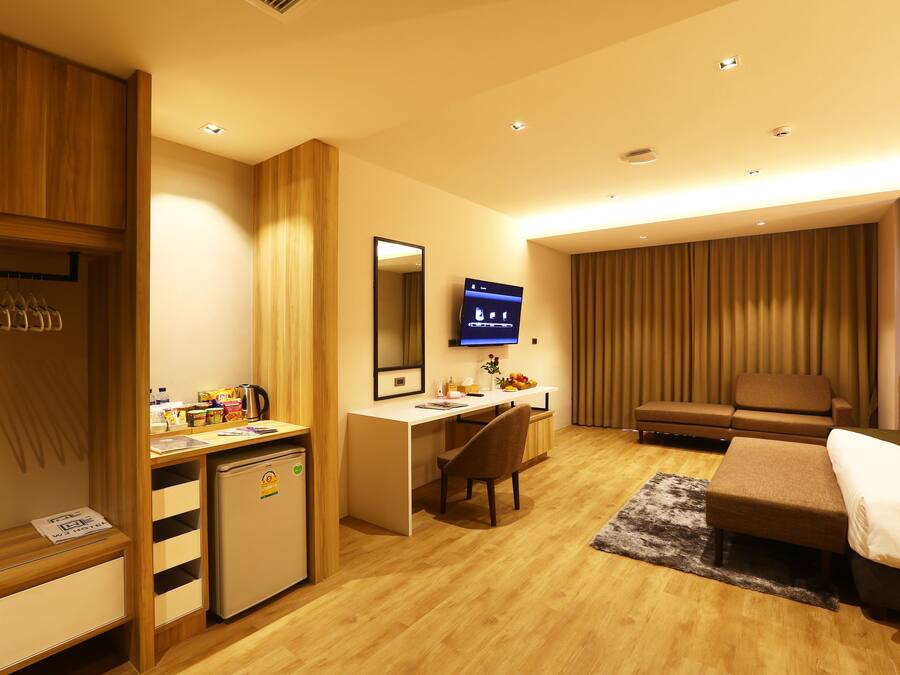 A hotel room with a wooden desk, a small refrigerator, a television, a sofa, and a bed.