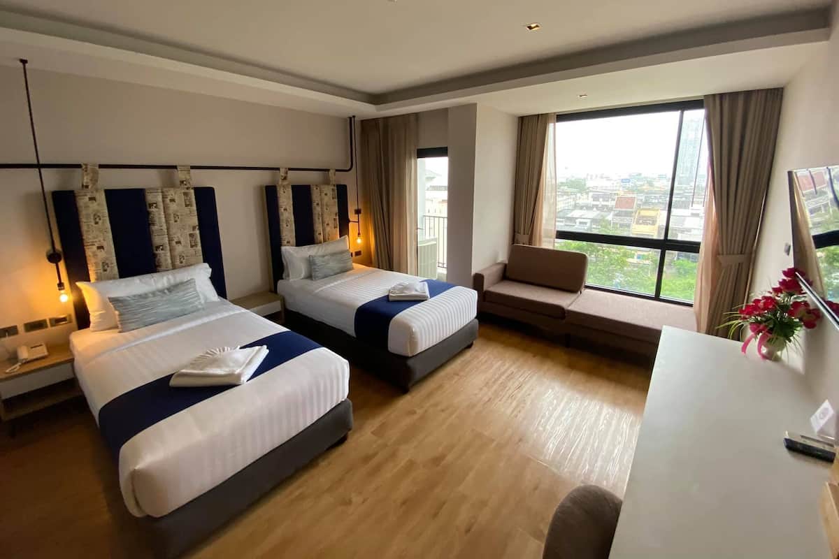 A hotel room with two beds, a desk, a chair, and a large window with a city view.