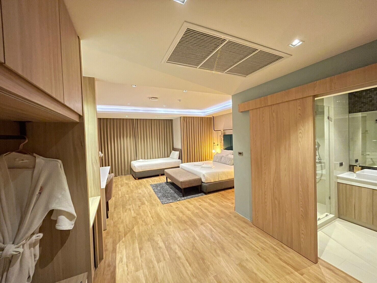 A modern hotel room with a wooden floor, two beds, a walk-in closet, and a glass shower area.