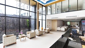 Un vestíbulo amplio con mostrador de recepción, zona de estar y grandes ventanales que ofrecen vistas al exterior.