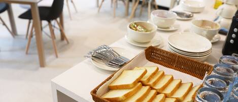 A buffet setup with bread, bowls, plates, and utensils.
