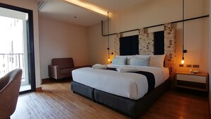 Habitación de hotel moderna con una cama grande, una silla, una mesita de noche y vistas al exterior.