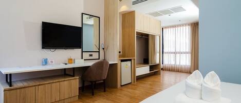 A hotel room with a bed, a desk with a chair, a television, a wardrobe, and a mirror.