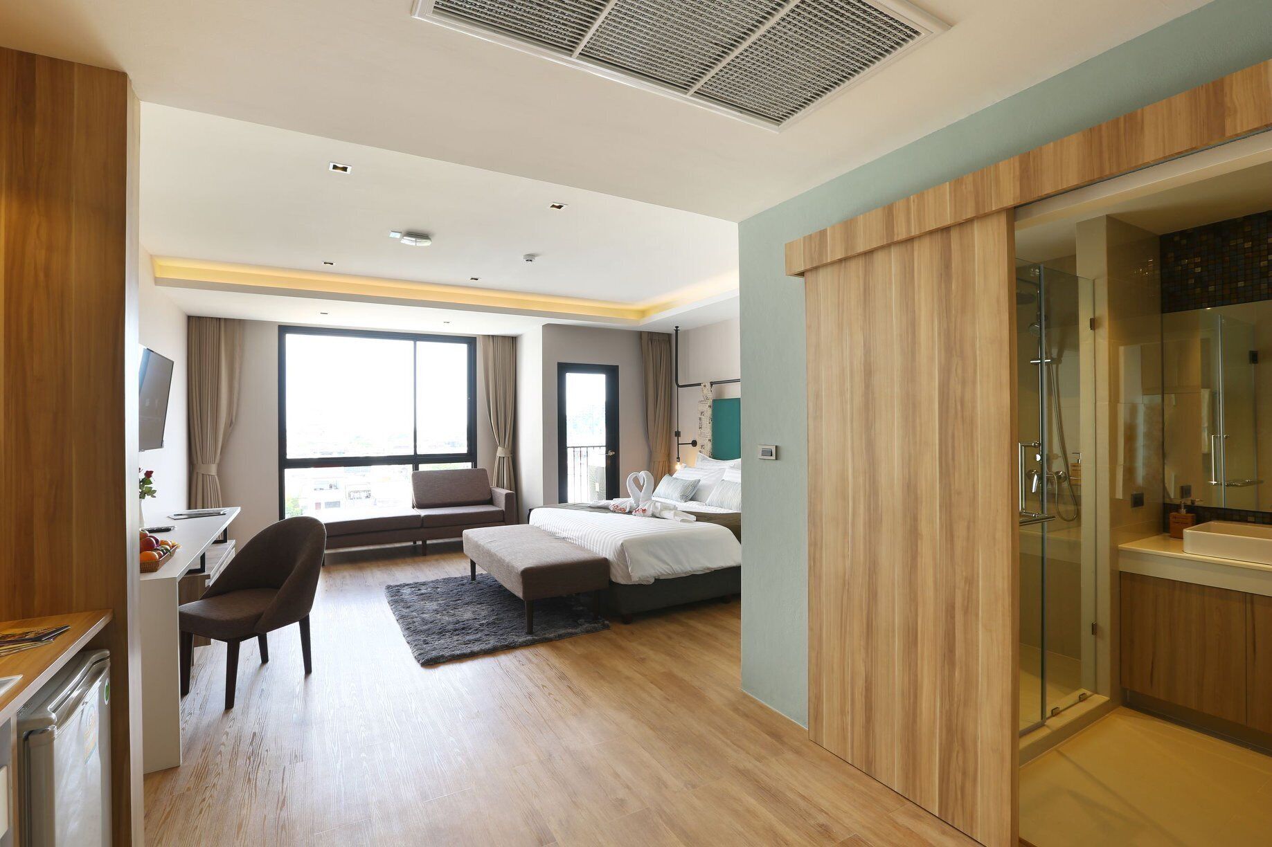 A modern hotel room with a bed, a desk, a chair, and a bathroom with a glass shower.
