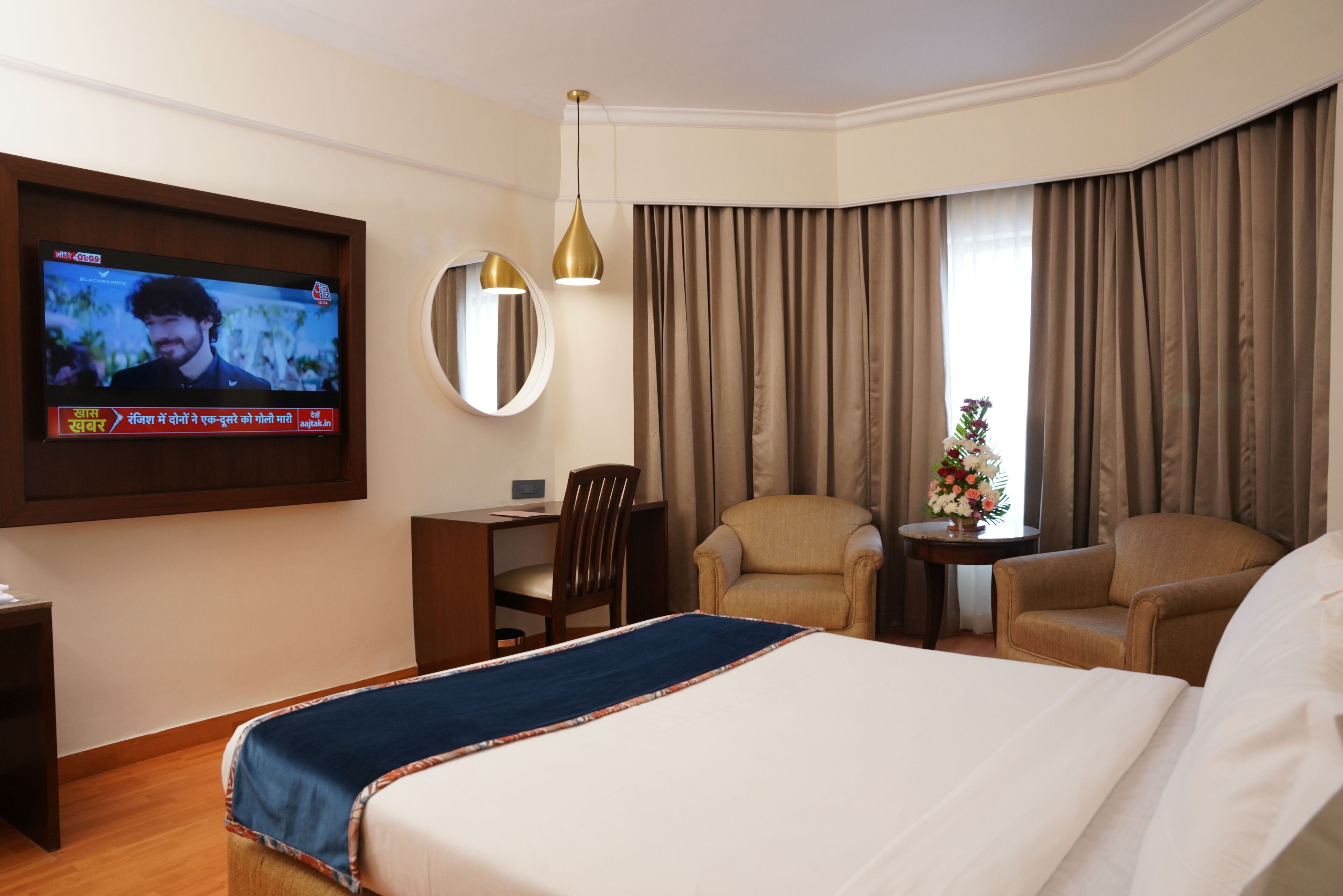 Una habitació d'hotel amb un llit gran, una taula de treball, dos seients còmodes, un televisor fixat a la paret i una finestra amb cortines.