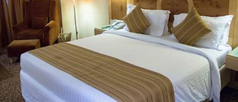 Quarto de hotel com uma cama grande, uma cadeira, uma mesa de cabeceira e um abajur.