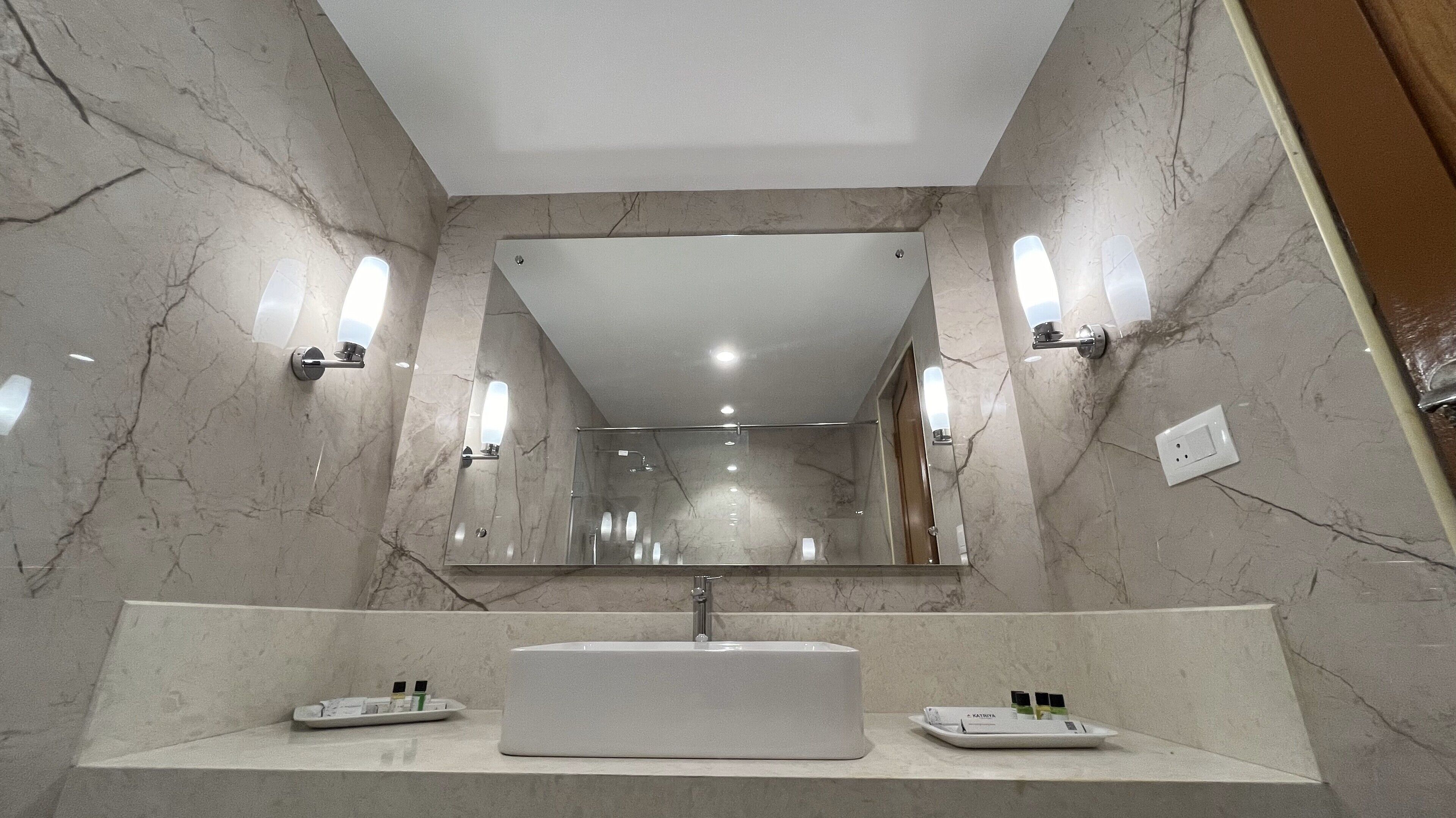 A modern bathroom with a large mirror, two sinks, and marble walls.