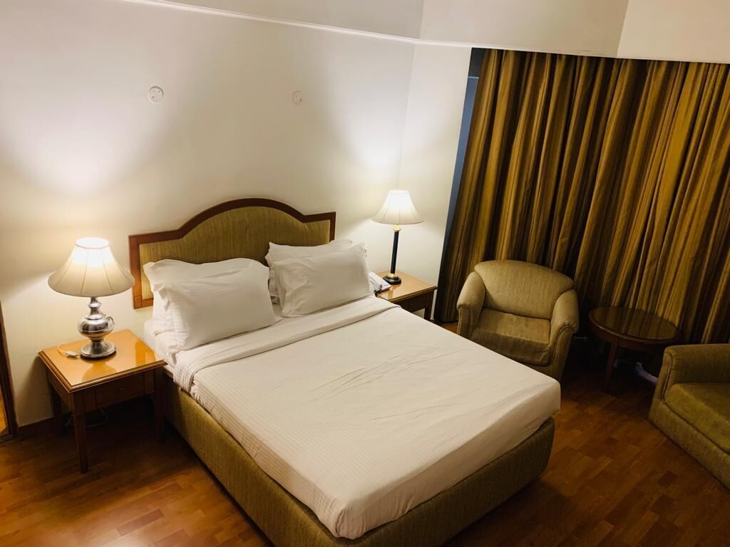 A hotel room with a bed, two bedside lamps, a chair, and a curtain.