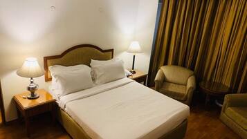 A hotel room with a bed, two bedside lamps, a chair, and a curtain.