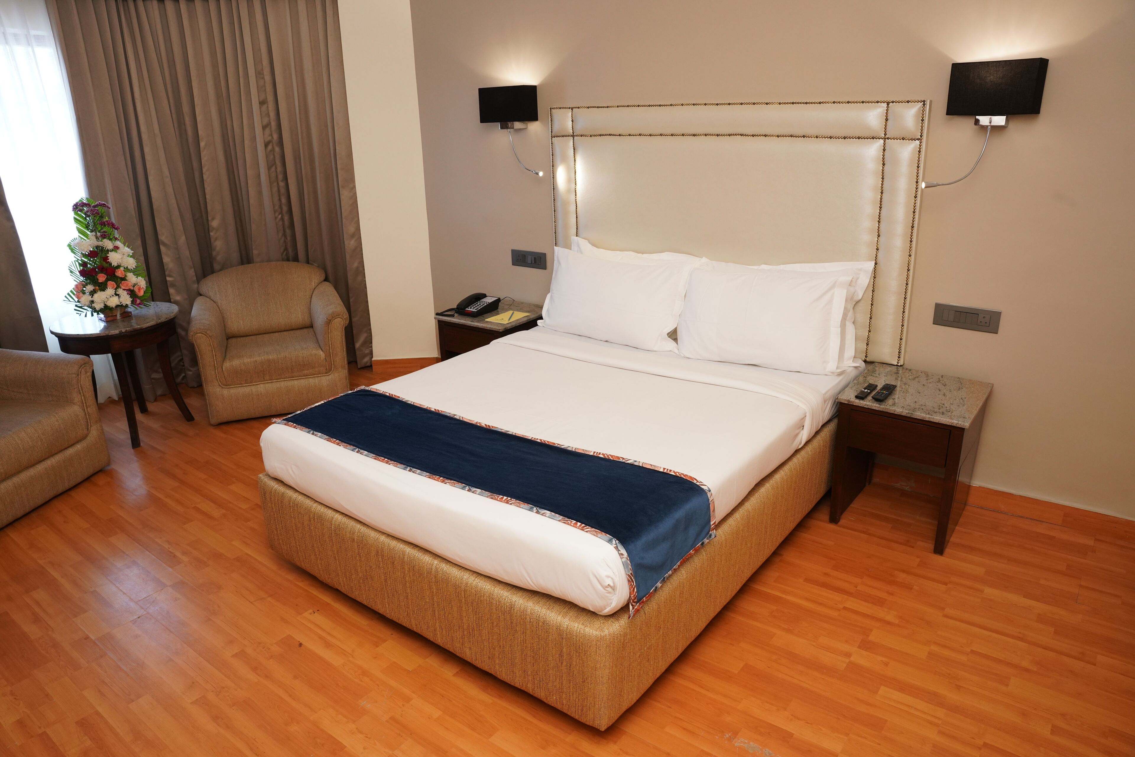A hotel room with a large bed, a chair, a nightstand with a phone, and a wall-mounted light.