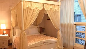 A four-poster canopy bed with a lace bedspread, a nightstand with a lamp, and a view of the city through a window with a decorative grille. - Riverbank Cottage (Wujie)