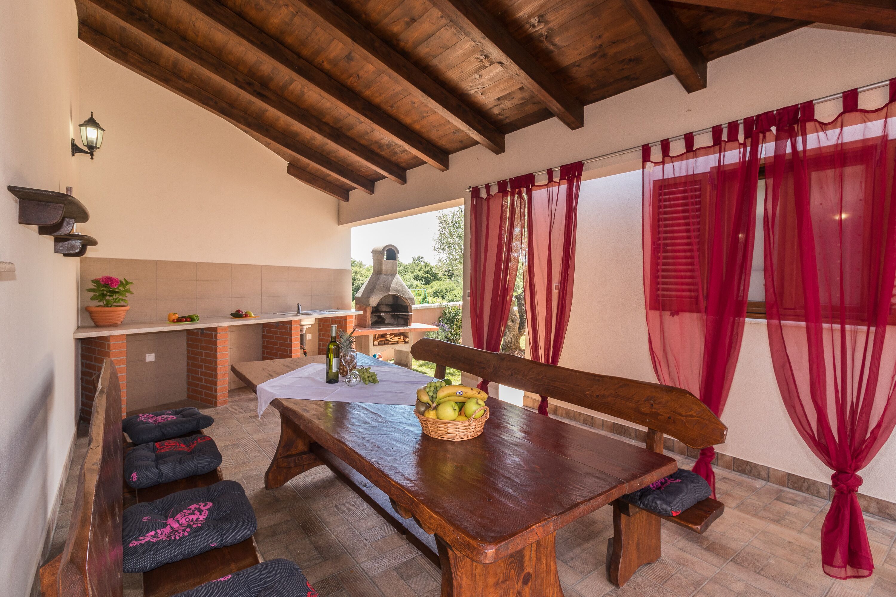A rustic outdoor dining area with a wooden table, benches, and a basket of fruit.