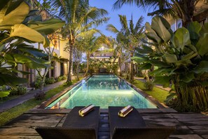 A pool area with lounge chairs and a clear view of a building in the background. - Sunrise Suite Seminyak (Denpasar)