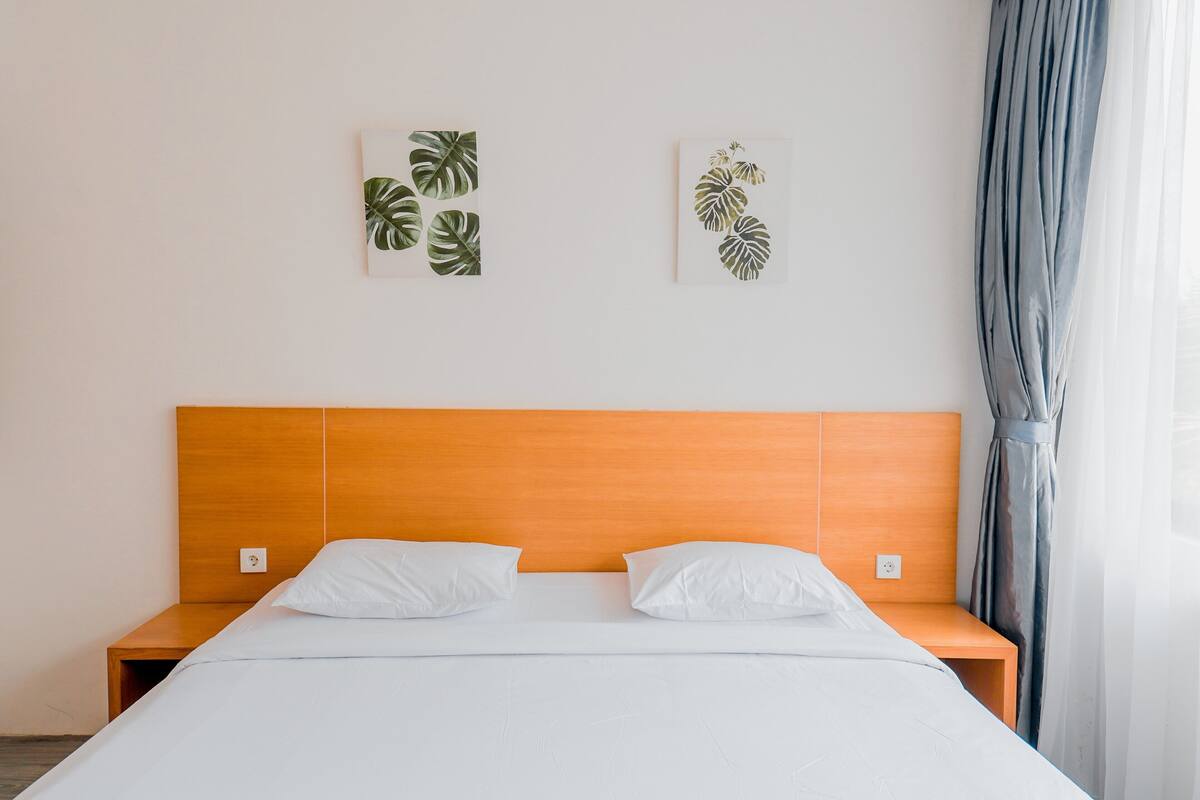 Una cama bien hecha con ropa de cama y almohadas blancas, un cabecero de madera y dos obras de arte con motivos vegetales colgadas en la pared.