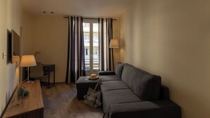 Une pièce de taille modeste, comprenant un canapé, une petite table et une chaise. Deux lampes sont placées de part et d’autre du canapé.
