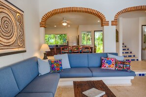 A living room with a blue sofa, colorful pillows, a wooden coffee table, and a ceiling fan.