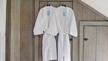 A room with wooden walls and a sloped ceiling. Two white robes are hung on a wooden door.