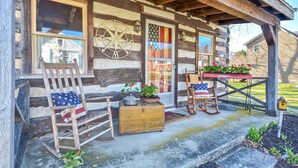 Ein rustikales Blockhaus mit Veranda, Holzschaukelstühlen, einem Tisch mit Topfpflanzen und einem Briefkasten.