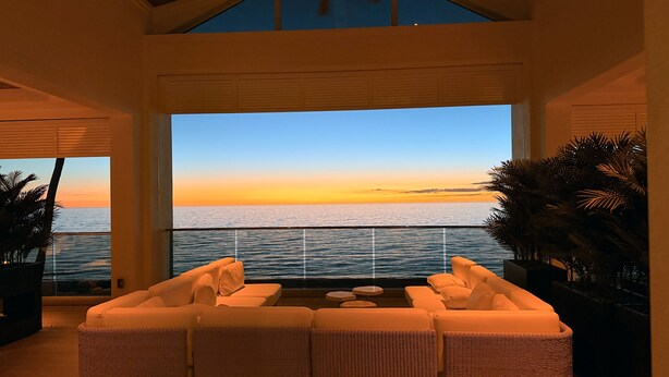 Ein geräumiger Balkon mit Blick auf das Meer bei Sonnenuntergang, möbliert mit Korbstühlen und einem Tisch.
