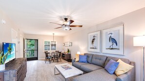 Ein modernes Wohnzimmer mit grauem Sofa, Couchtisch, Fernseher und Kunstwerken an der Wand.