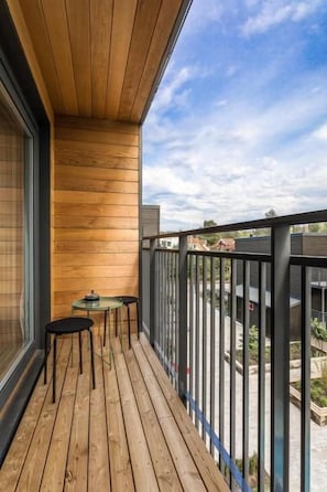 Une terrasse en bois avec une balustrade en verre, une petite table et deux chaises.