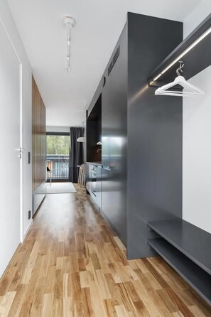A modern hallway with a wooden floor, a dark wall, and a hanging light fixture. - HOOM Home & Hotel Sollentuna (Sollentuna)
