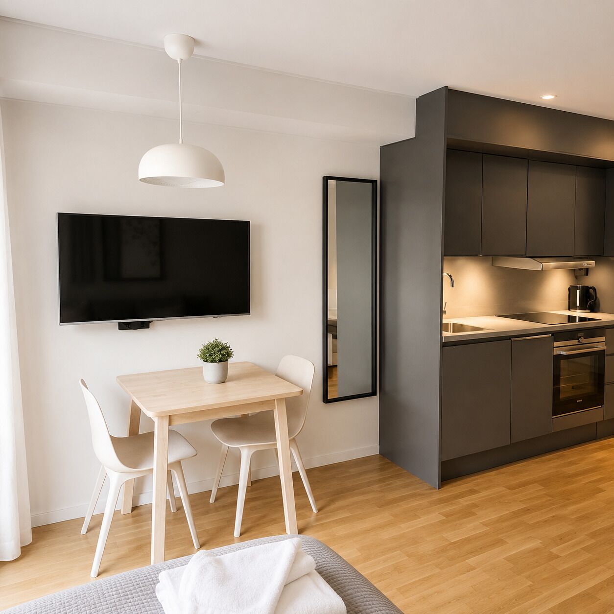 A modern kitchen with dark cabinets, a flat-screen TV, and a dining area with a table and chairs.