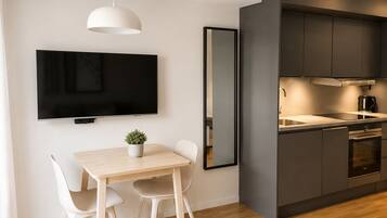 A modern kitchen with dark cabinets, a flat-screen TV, and a dining area with a table and chairs.