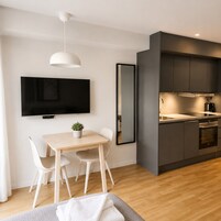 Une cuisine moderne avec des meubles de couleur sombre, un téléviseur à écran plat et un coin repas comprenant une table et des chaises.