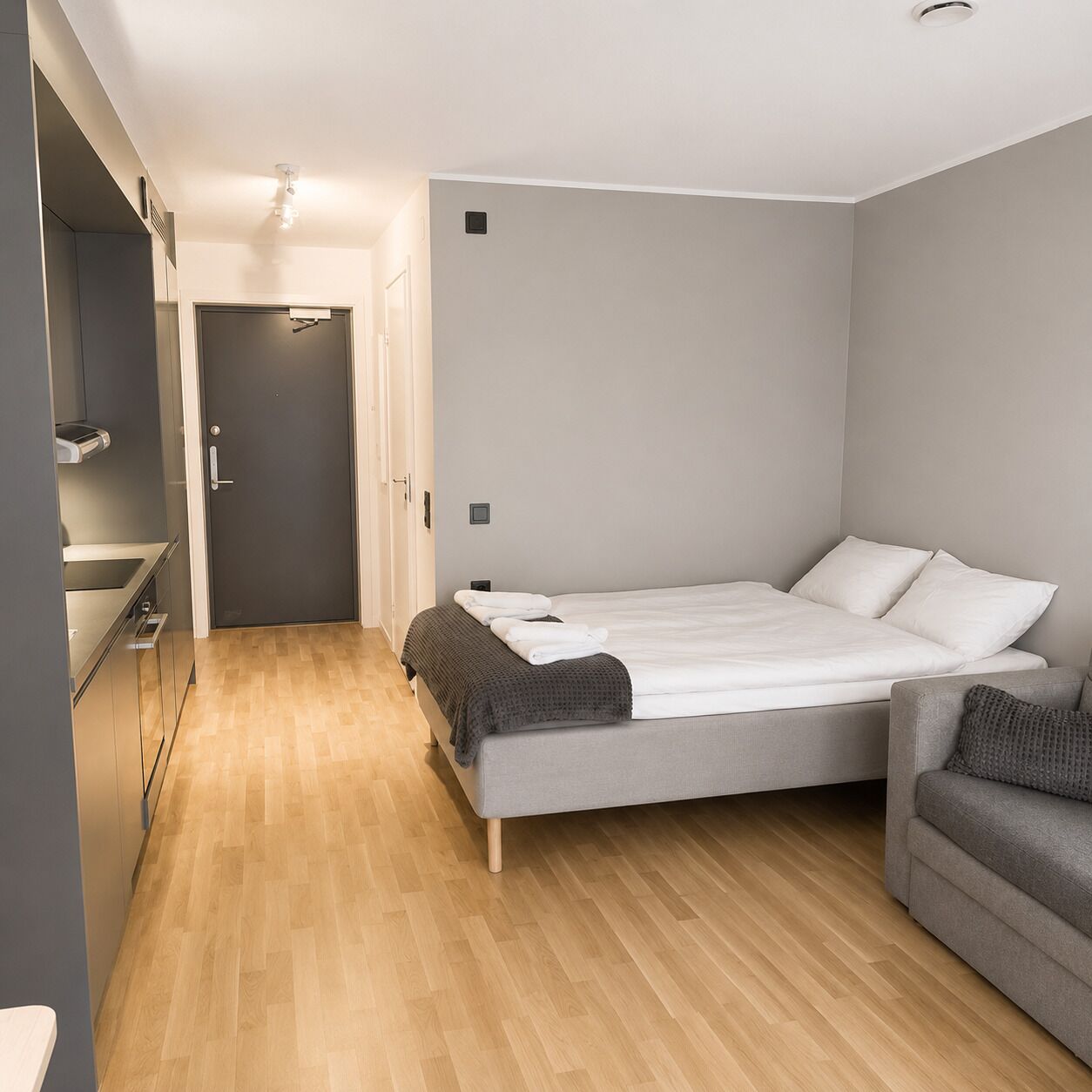A modern bedroom with a bed, a sofa, and a kitchenette area.