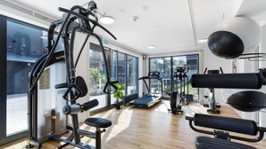 Een sportschool met trainingsapparatuur, grote ramen en een houten vloer.