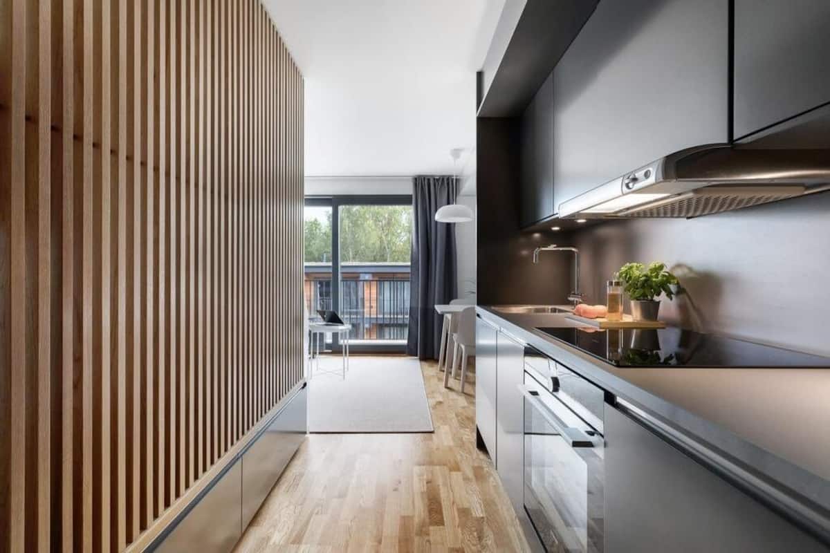 Una cocina moderna con separador de madera, electrodomésticos de acero inoxidable y vista a un balcón exterior.
